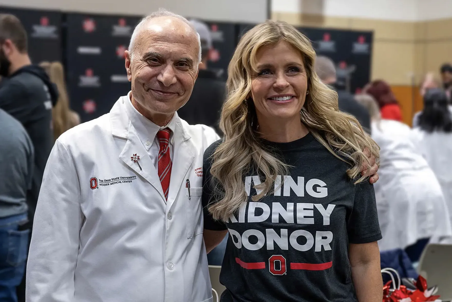 A doctor in his white coat and a donor wearing a T-shirt that says "Living kidney donor" smile as they pose for a photo.