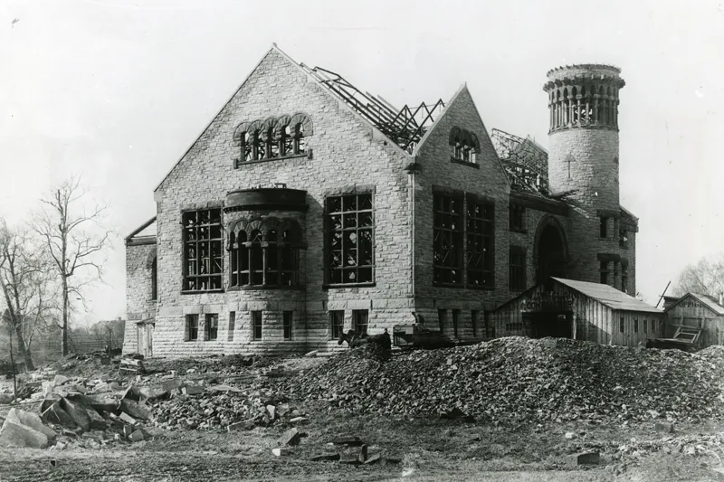 A black and white photo shows Orton Hall while it was under construction. Most of the stone walls are up but the roof is just framing. All of the land around it is empty.
