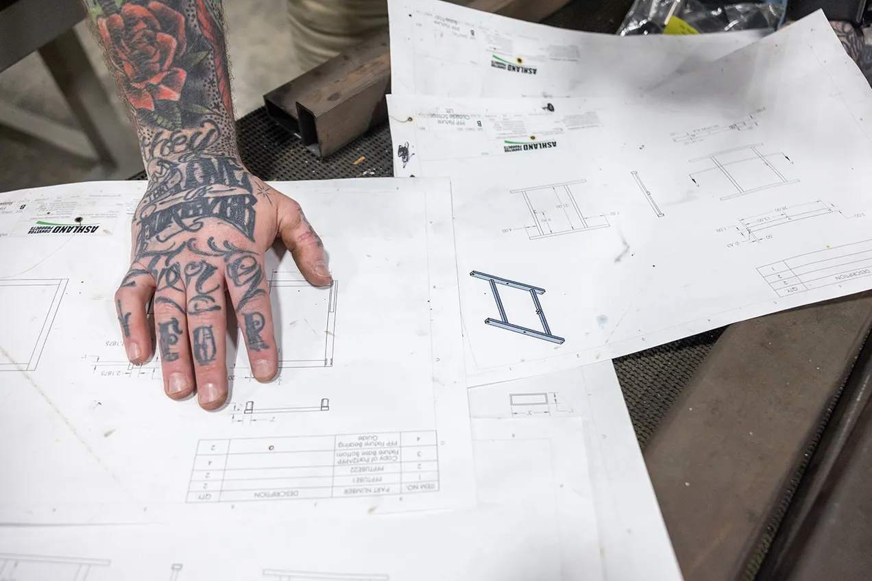 Zack looks over blue prints. This photo shows just those plans and his tattooed hand on them.