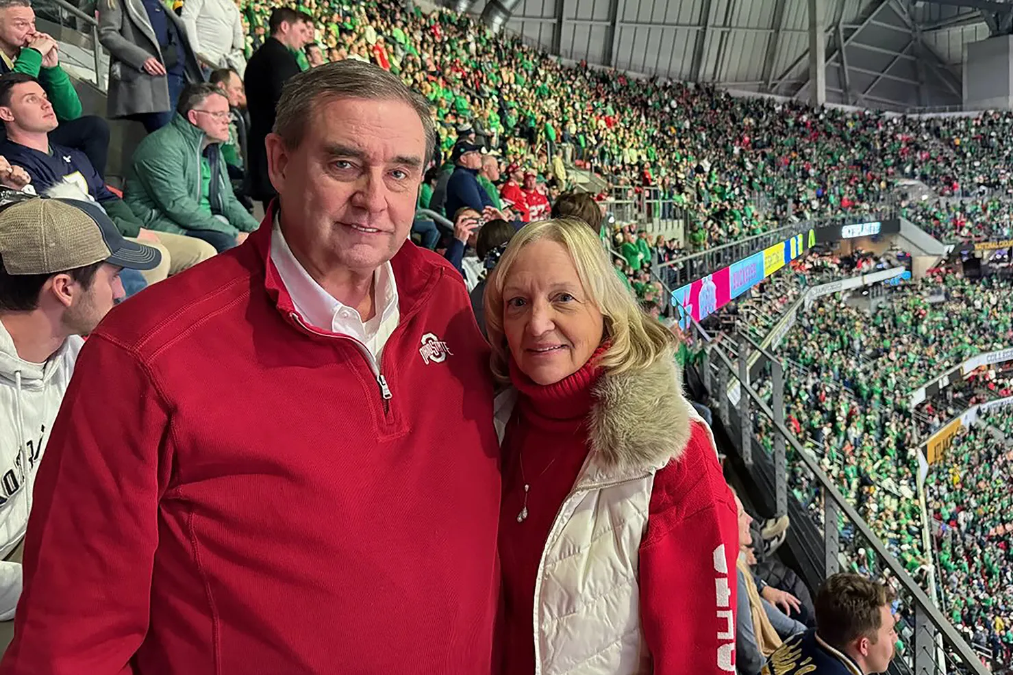 The same couple poses for another photo now. In a stadium filled with green-clad fans, they wear scarlet Ohio State gear.