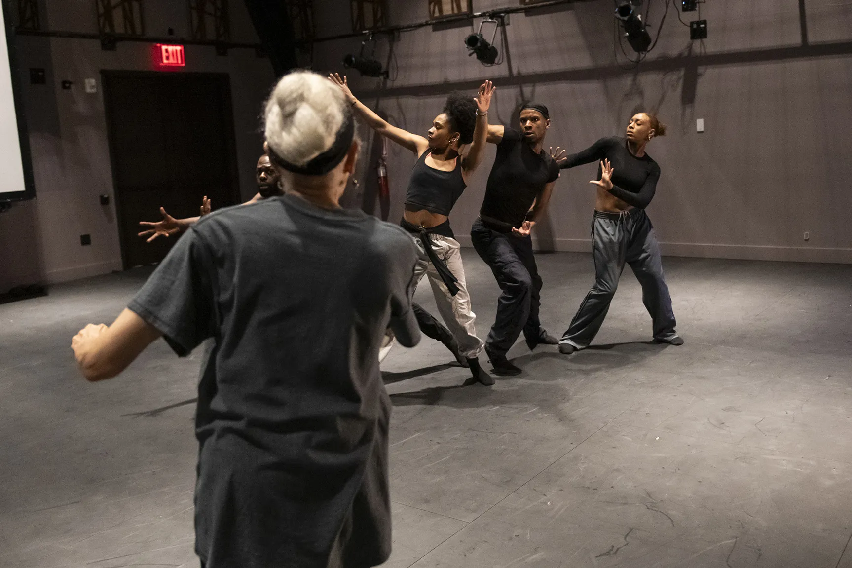 With her back to the camera, Dianne coaches four dancers who are in a row and each performing unique choreography.