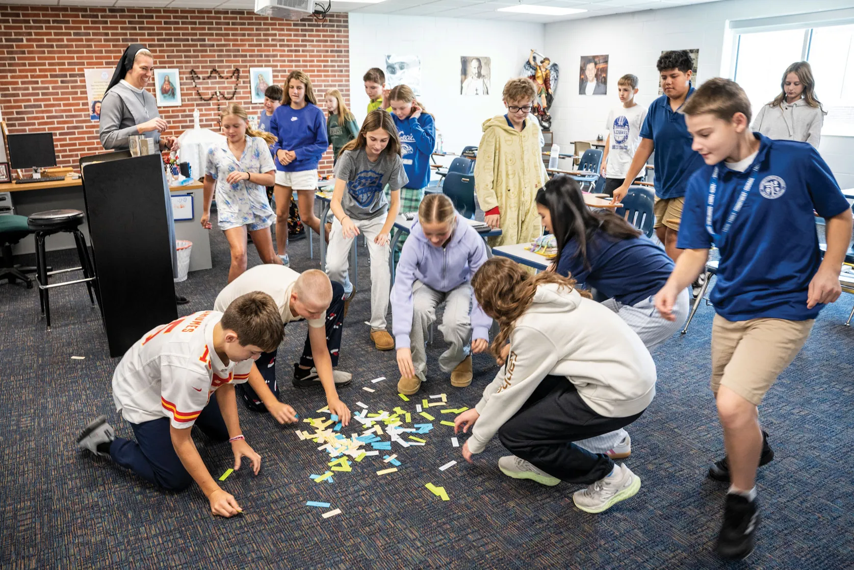Middle schoolers--some wearing school uniforms and some wearing pajamas for a school spirit day--stoop and gather around a pile of colored paper strips on the carpeted floor of a classroom.