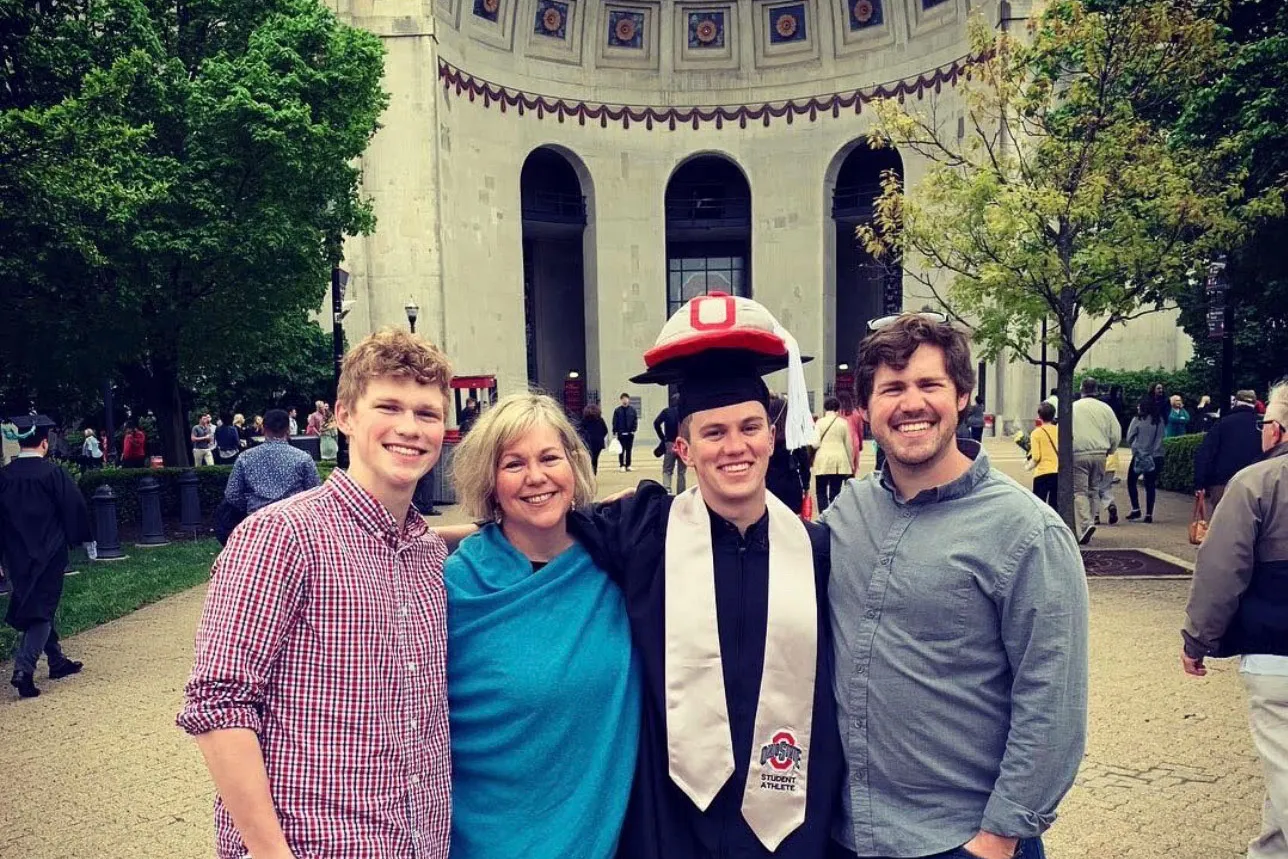 A graduate with Brutus gear stands outside Ohio Stadium with loved ones