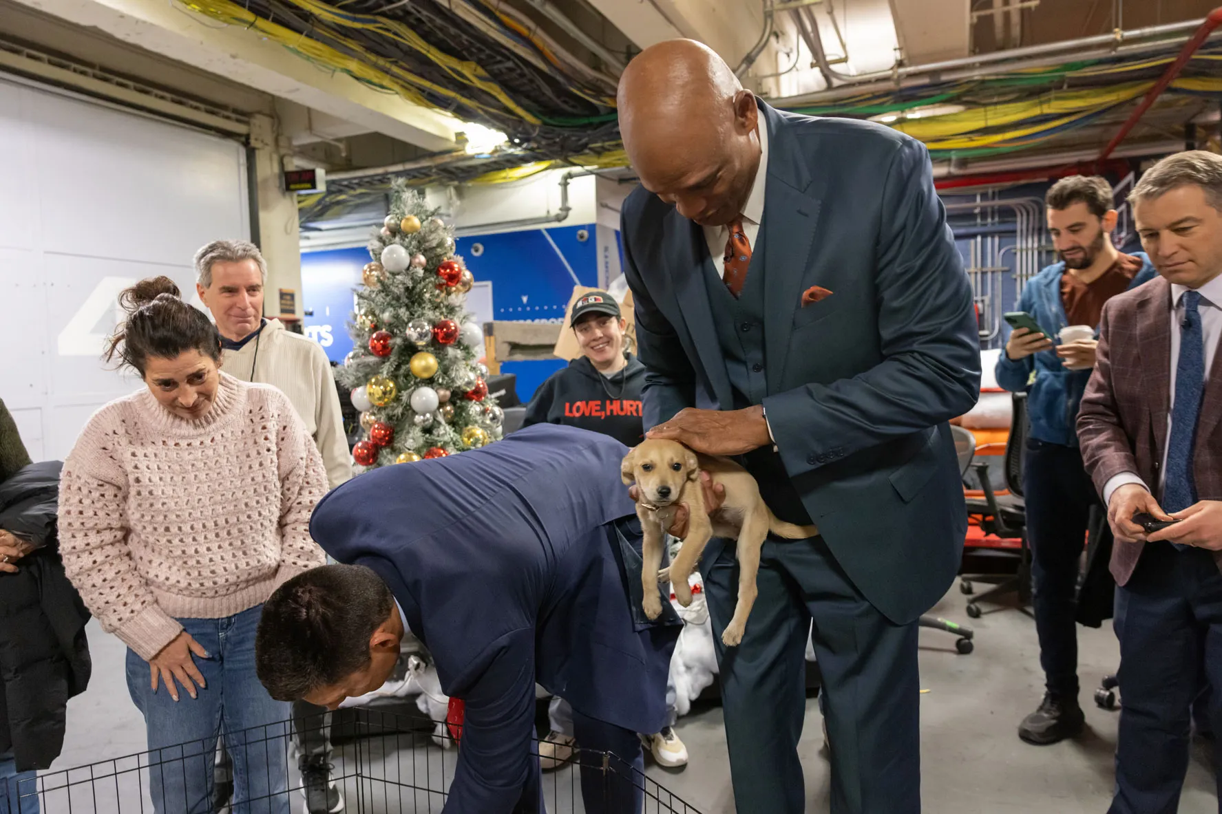 Kellogg has picked up a puppy from the enclosure and cradles it in his hands, looking down as he pets it.