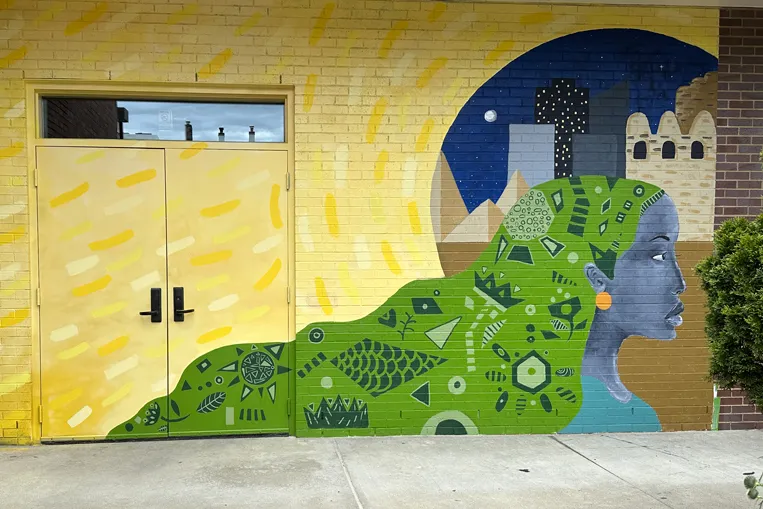 A mural painted on a brick building and over double doors shows a woman with trailing hair