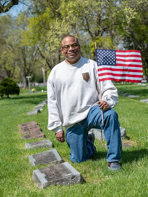 man kneeling next to gravestone holding american flag