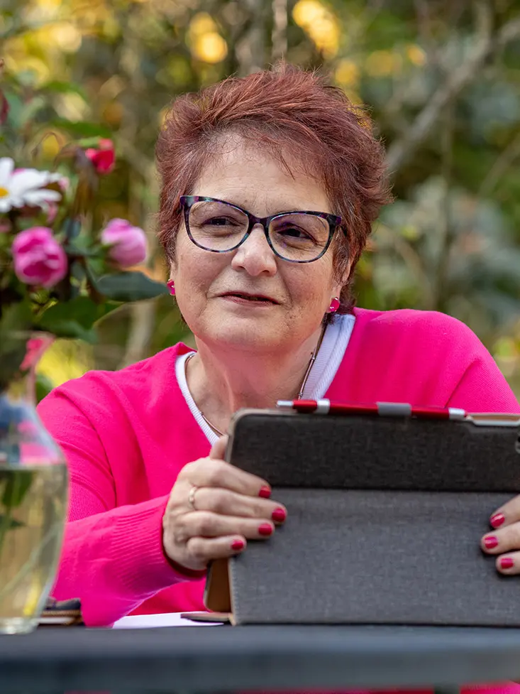 Electra Paskett is sitting outside near a rose bush. She is wearing a pink sweater 