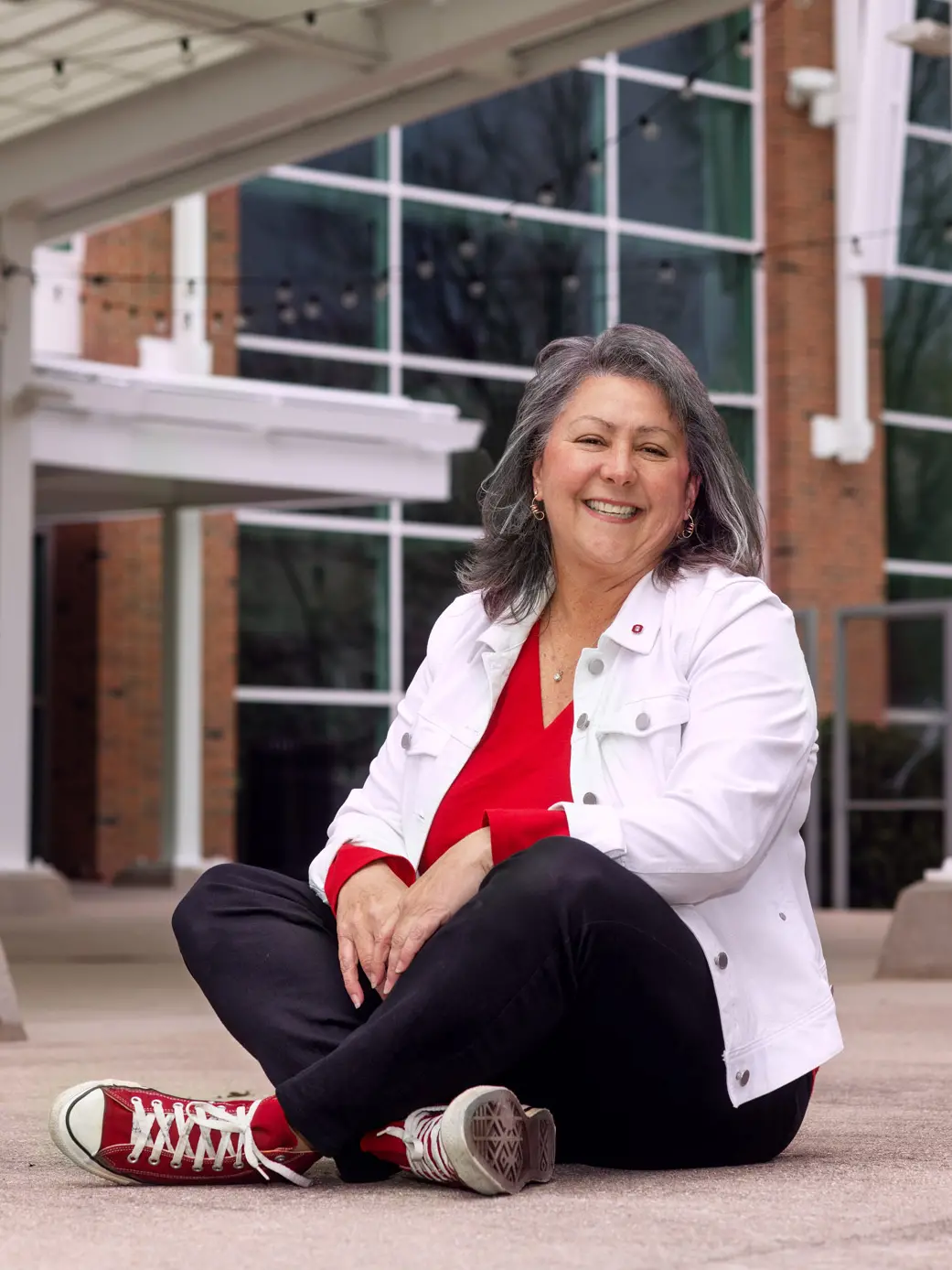 Smiling woman sits cross-legged on the ground in front of Longaberger Alumni House