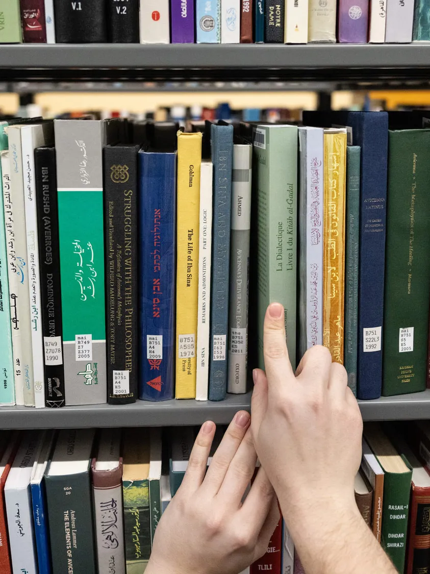 A closeup look at books on shelves show three rows of them and hands (with chipped nail polish) sliding one book into place. 