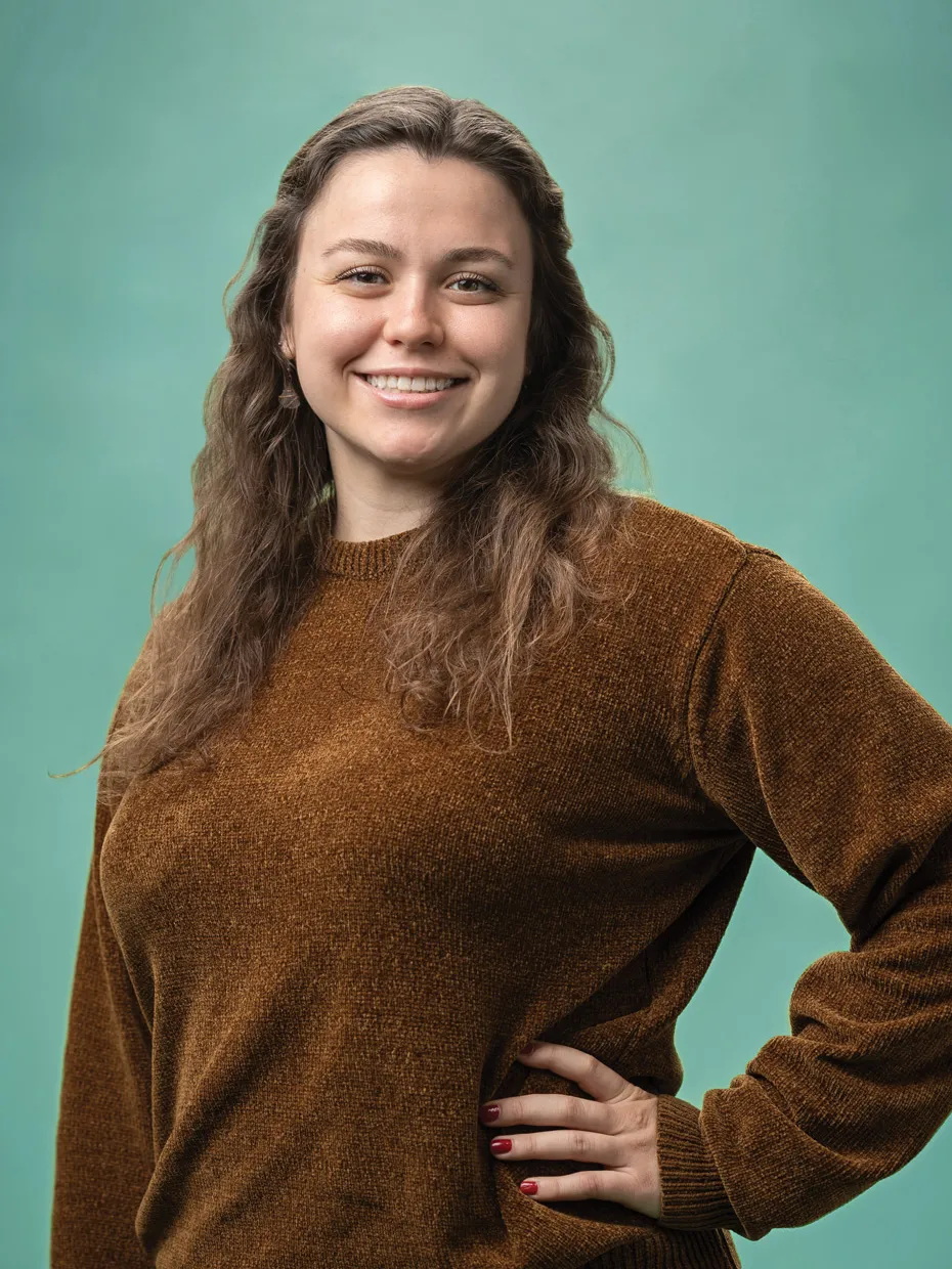 A smiling young woman poses with one hand on her hip.