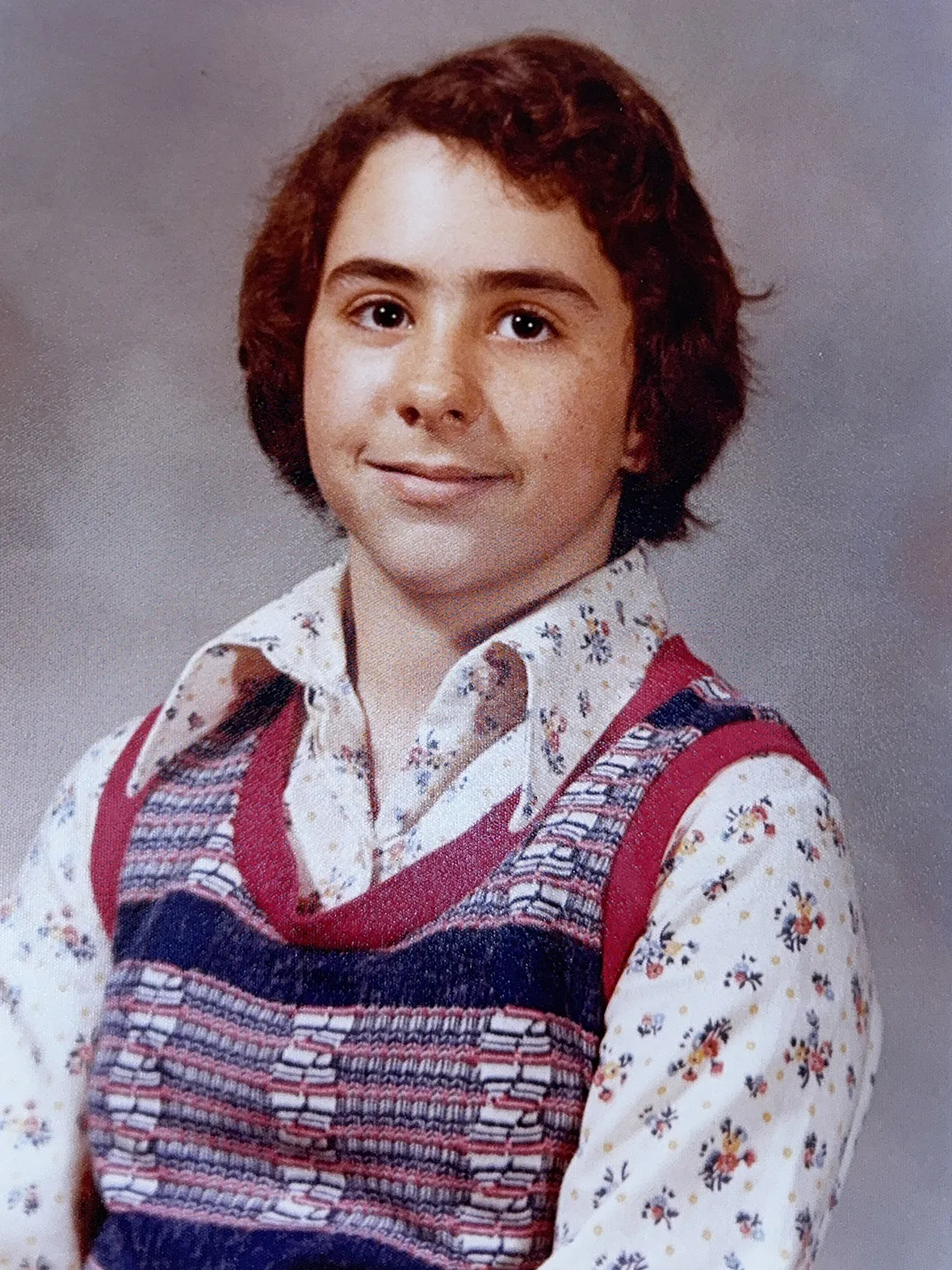 Molly in middle school has pretty eyes and an unfortunate haircut. Her shirt is flowered and her vest has a woven geometric pattern.