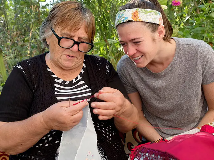 woman stitches embroidery as a younger female watches