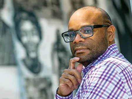 Headshot of Trevon Logan, bald Black man with glasses, wearing checked button up shirt