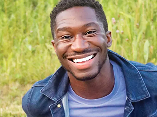 portrait of a black man smiling with a purple shirt and denim jacket on