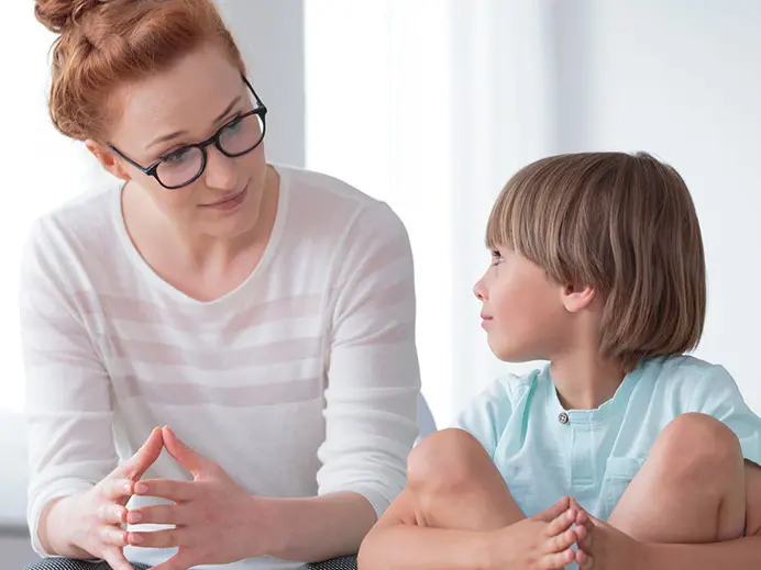 A woman with red hair and glasses is leaning on a table next to a young child