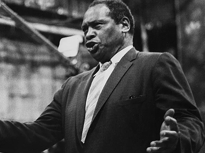 Black and white historic photo of Paul Robeson. He is singing with his arms slightly raised to the sides.