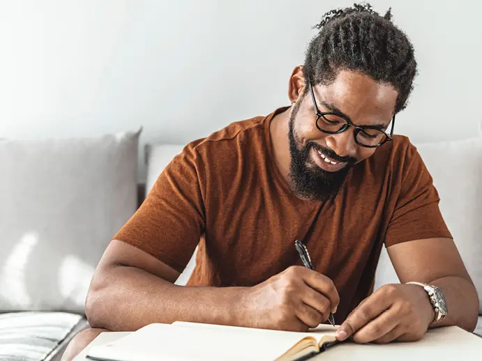 Man wearing glasses and smiling writing in a notebook