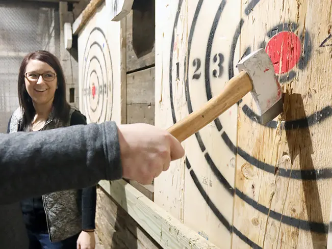 Man smiling while pulling out an axe he threw towards a bullseye