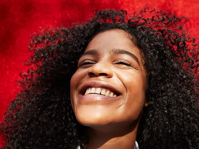woman with curly hair smiling with a bright red background