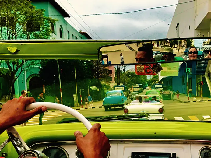 bright green colored cuban cab with people seen in the rear view mirror