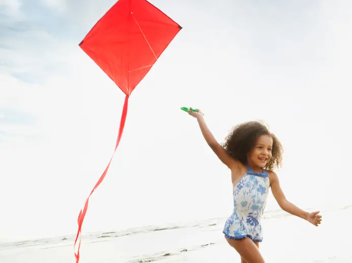 young girl in swimsuit flying a red kite on the beach