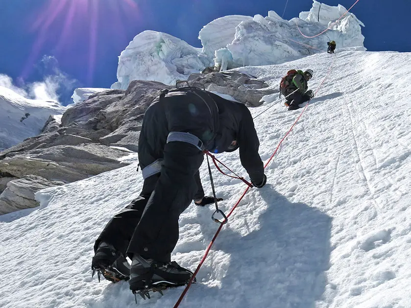 three men climbing up the side of a snow capped mountain