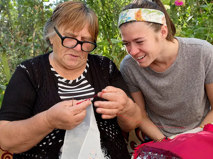 woman stitches embroidery as a younger female watches