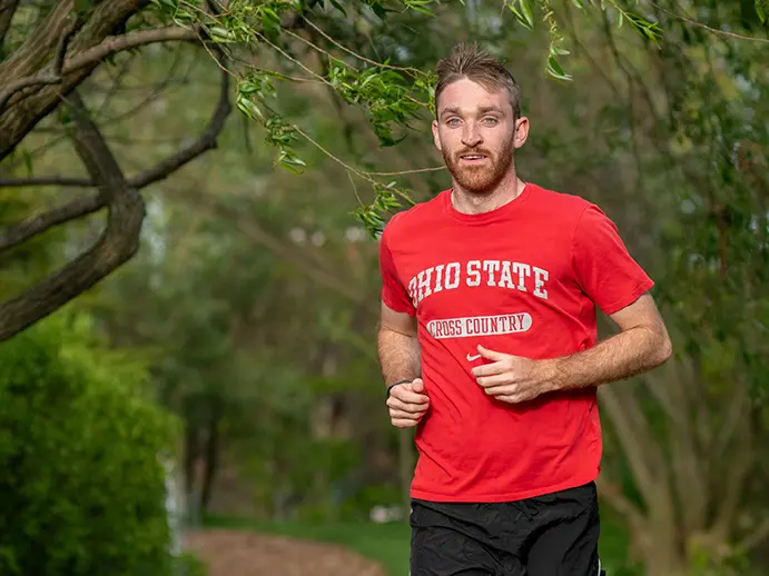 Ohio State cross country athlete runs along a wooded path 