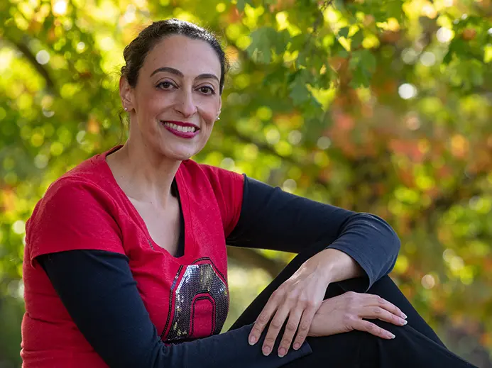Portrait of Rosa Ailabouni sitting outside wearing a red Ohio State shirt, a black long sleeve shirt, and black pants