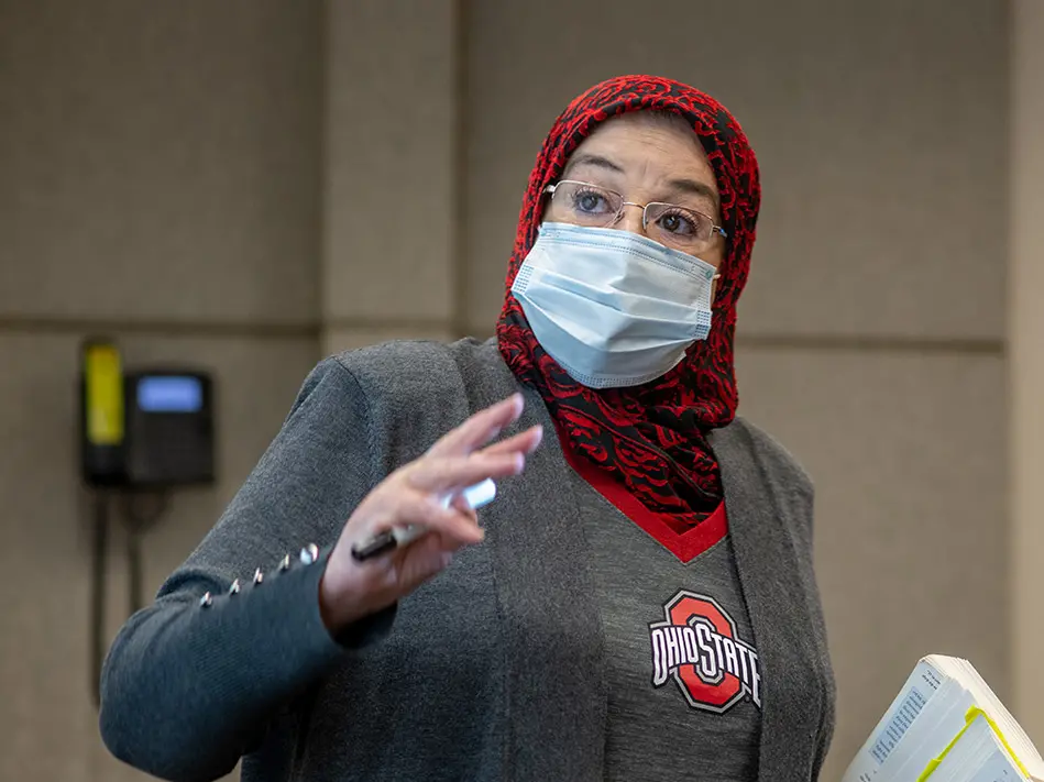 Female professor wearing red head scarf and mask gestures with her hand