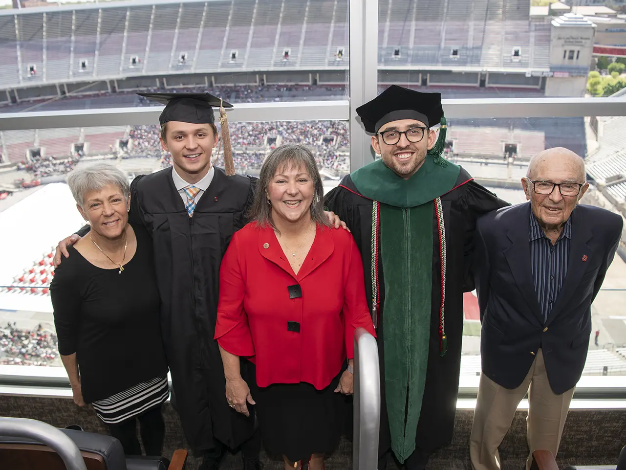 In a photo of a family, two young men wear graduation caps, gowns and smiles, as their mom, aunt and grandpa stand proudly by their sides.