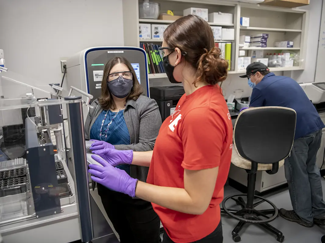 three people in a lab setting wearing personal protection equipment