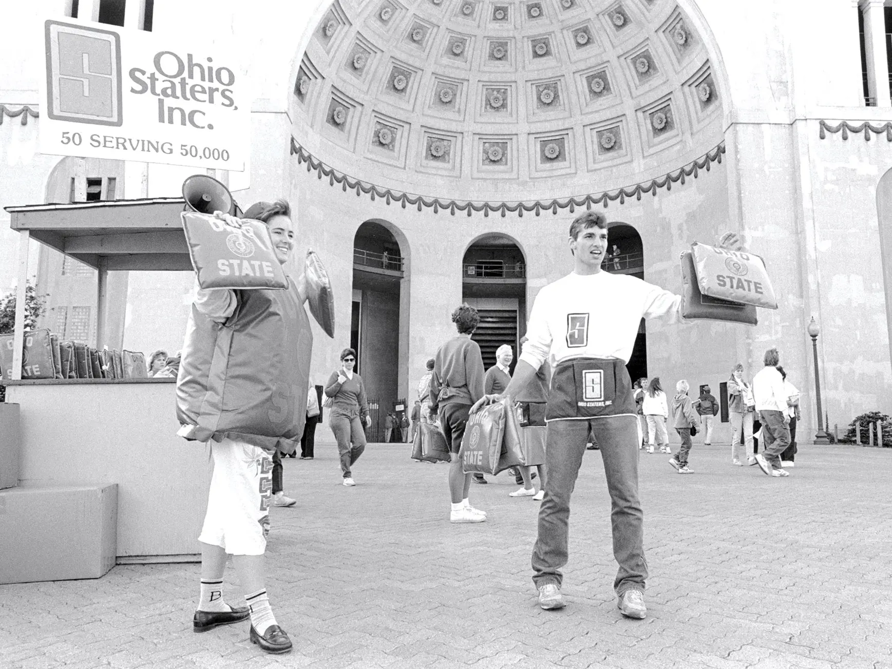 man and a woman handing out seat cushions to spectators in front of ohio stadium