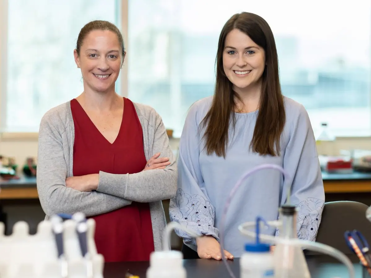 Two women smile in a lab setting.