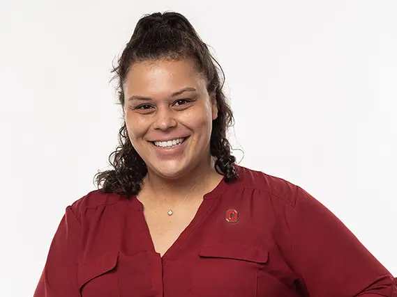 A biracial woman with a friendly smile poses on a chair.