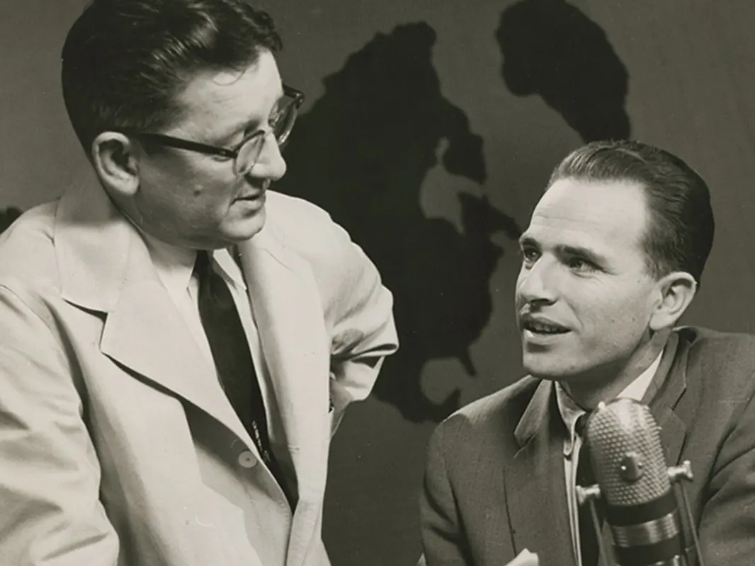 A young Don Quayle seated at a radio broadcast microphone looks up at a doctor Samuel Sander