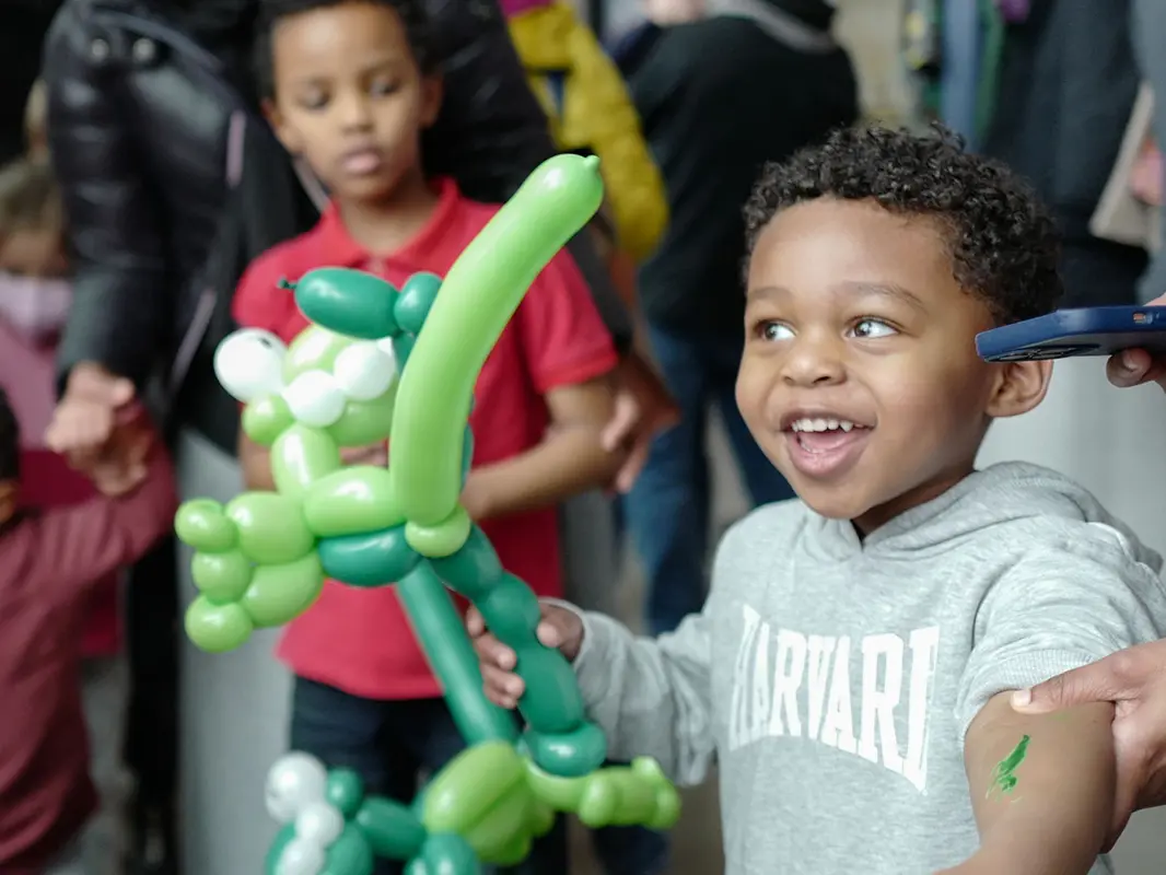 A toddler is all smiles while holding a unique balloon animal