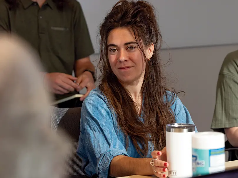 A white woman with long brown hair looks interested while listening in a meeting. 