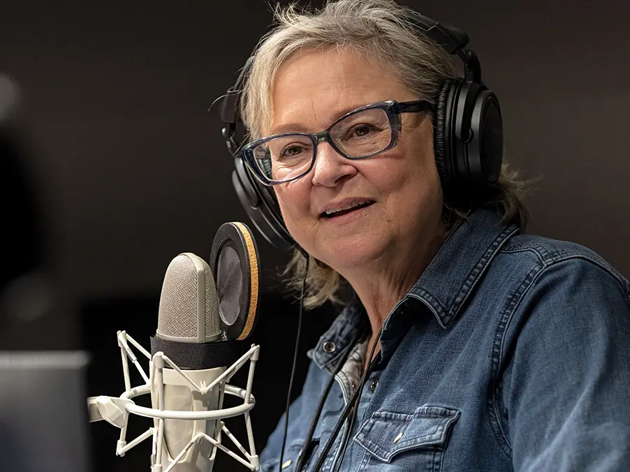 Radio host Ann Fisher smiles behind a microphone 