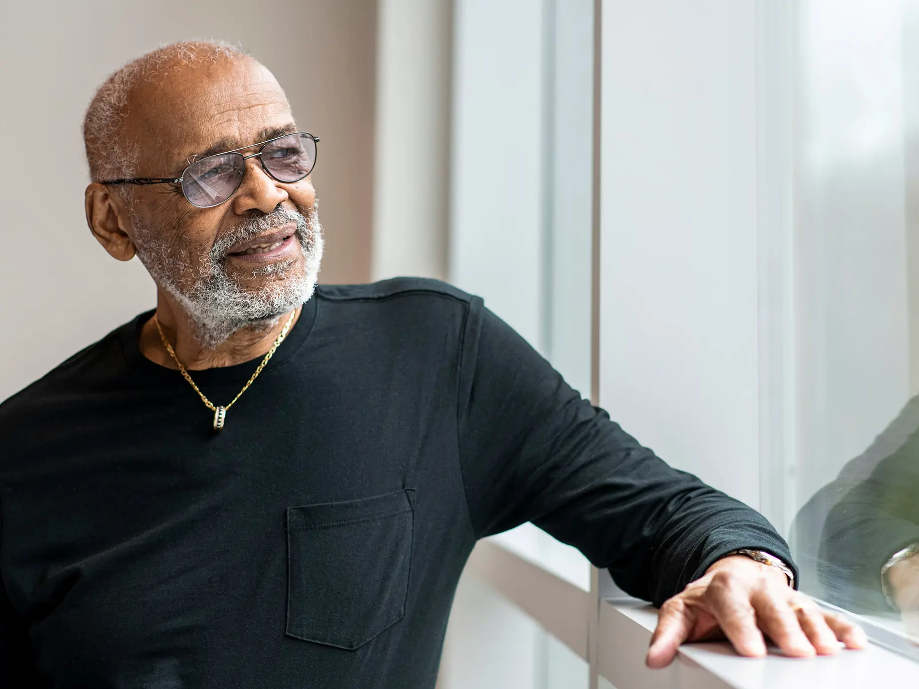 An older black man with gray hair and glasses seems thoughtful as he looks into the distance