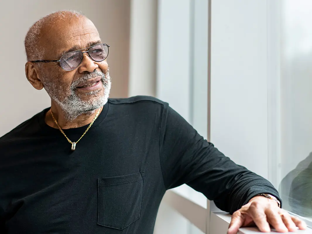 An older black man with gray hair and glasses seems thoughtful as he looks into the distance.