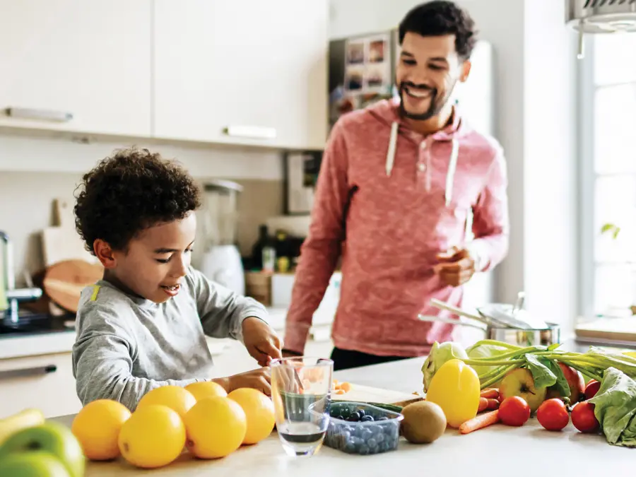 A father and son enjoy preparing fruits and vegetables at the island in their kitchen.