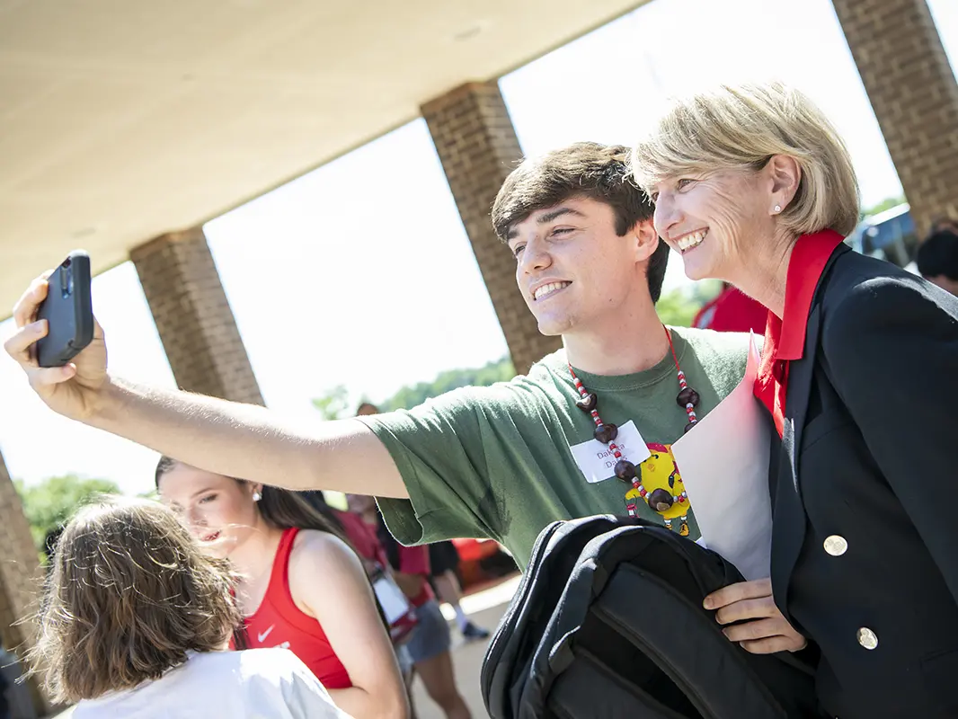 Ohio State President Kristina M. Johnson, a white woman with short blond hair, smiles and poses for the camera with a student