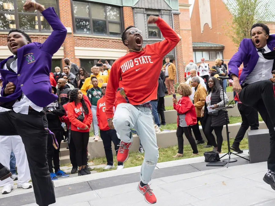 Several young Black men dancing in step and have big smiles and animated expressions