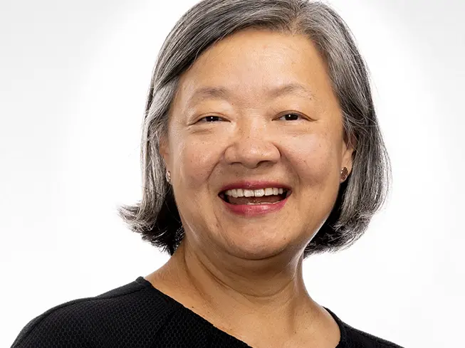 An Asian woman with chin-length hair stands comfortably and confidently with a smile that lights up her face.