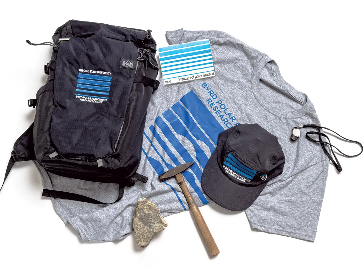 A T-shirt, backpack and baseball cap are each adorned with variations of a logo that is a rectangle of bars of blue with space between them. The bars vary in depth and are usually thicker at top. They could be seen as sky over a glacier or different layers of a glacier. Also shown are rocks, a hammer and a mug of tea.