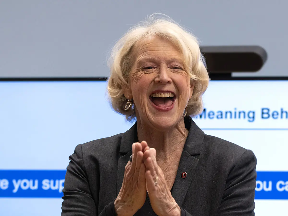 An older white woman smiles broadly and holds her hands together in front as if she may be clapping enthusiastically
