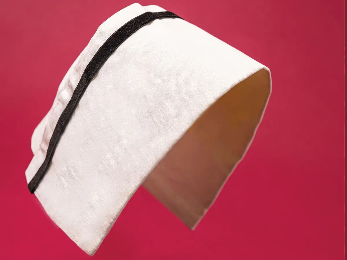 A whiteish rectangle of fabric, with a black velvet ribbon a quarter of an inch from the top, is shown arched as if on top of a nurse’s head.