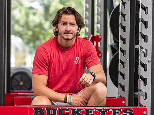 Anthony Dujmovic, a young man in a T-shirt and shorts, looks straight into the camera with a slight smile. His pose and expression make him seem confident and smart.