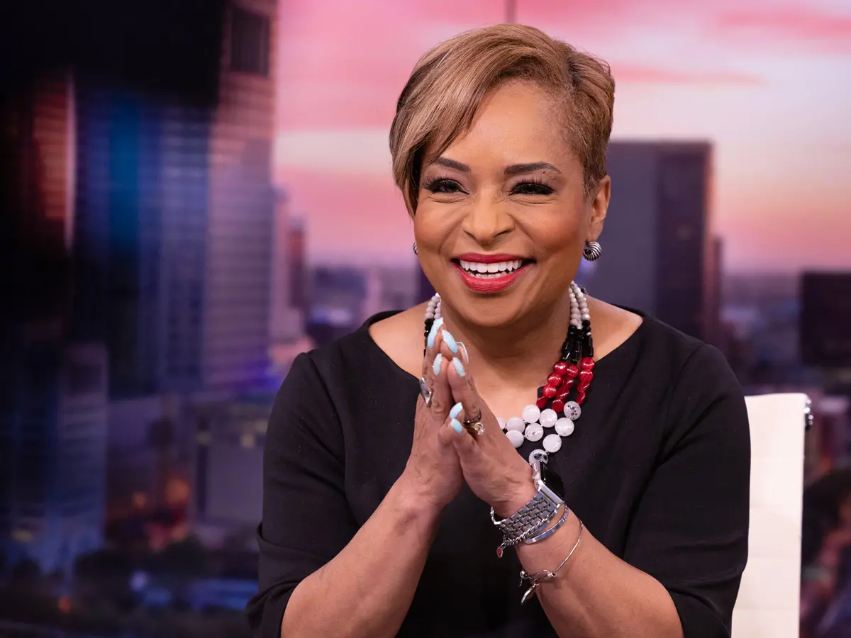 Tracy Townsend, an attractive woman with symmetrical features and bright lipstick, smiles as she looks at a camera during the newscast. The background is a picture of a sunrise over Columbus. 